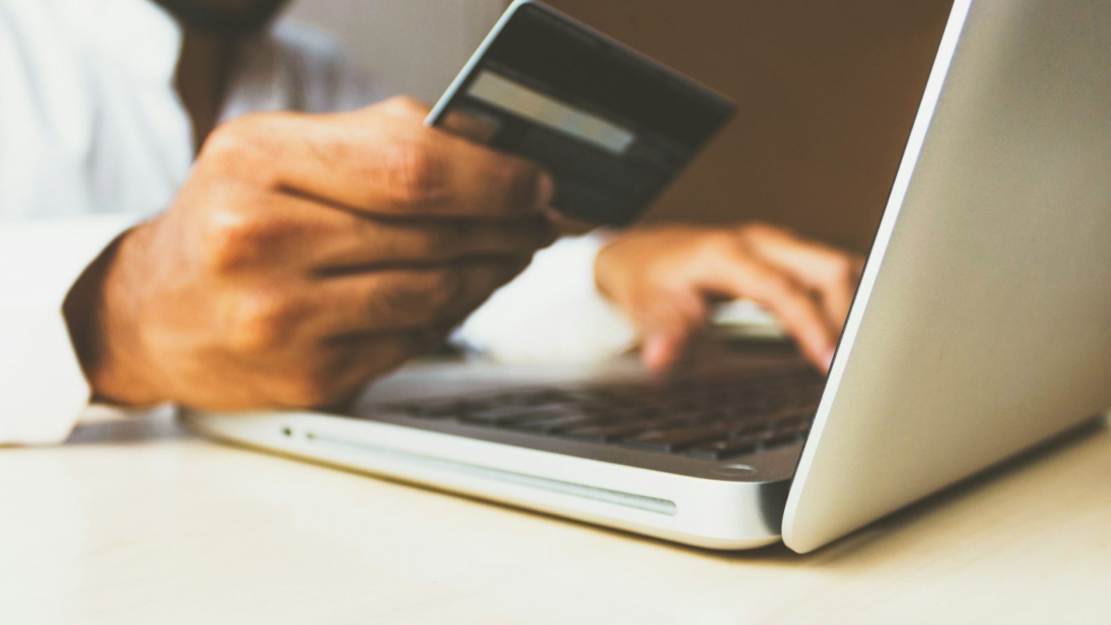 A person holding a payment card while using a laptop.